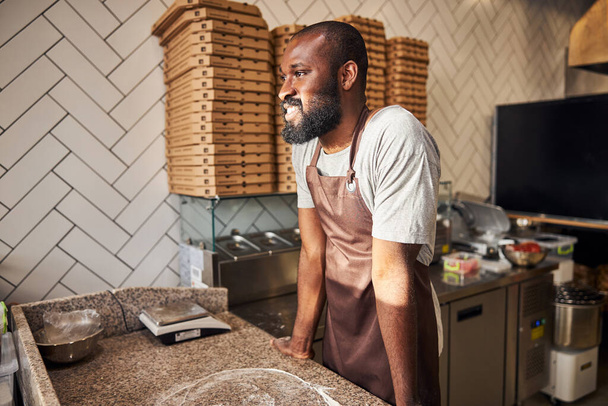 Cheerful man enjoying making pizza in cafe - Фото, зображення