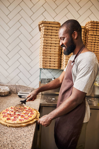 Vidám fiatalember vágás pepperoni pizza pizzériában - Fotó, kép