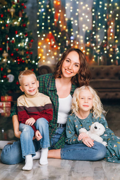 Cute mother with daughter and son posing at the Christmas tree. Happy new year concept. Toning. - Foto, Imagem