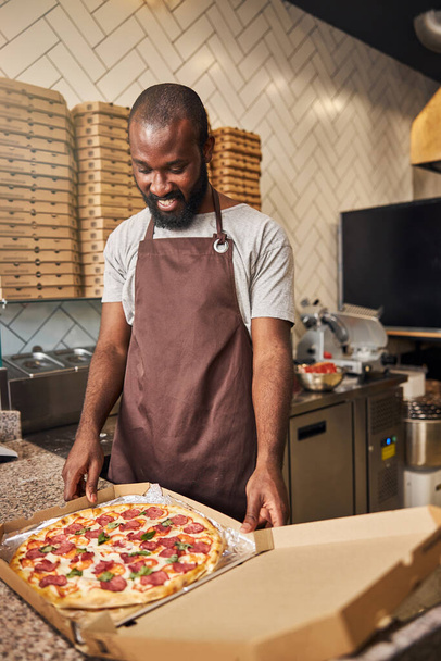Handsome Afro American man standing at the counter with pizza - Photo, image