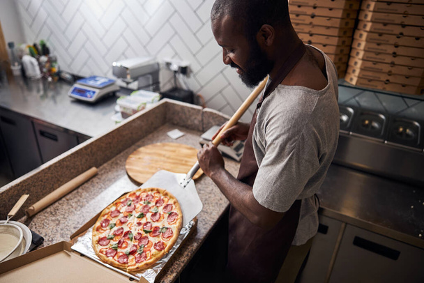 Przystojny młody człowiek umieszczając pizzę pepperoni w papierowym pudełku - Zdjęcie, obraz
