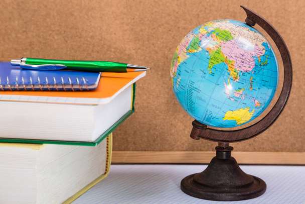 Globe, books and notebooks with pen on the table - Фото, изображение