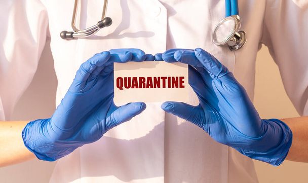 word QUARANTINE on paper in hands of doctor in protective gloves over white background. medical lockdown concept - Фото, изображение