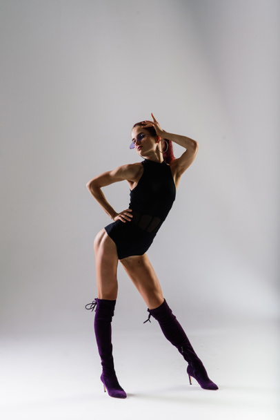 Joven hermosa hembra flexible en un mono negro y tacones altos está posando en un estudio de baile. - Foto, Imagen