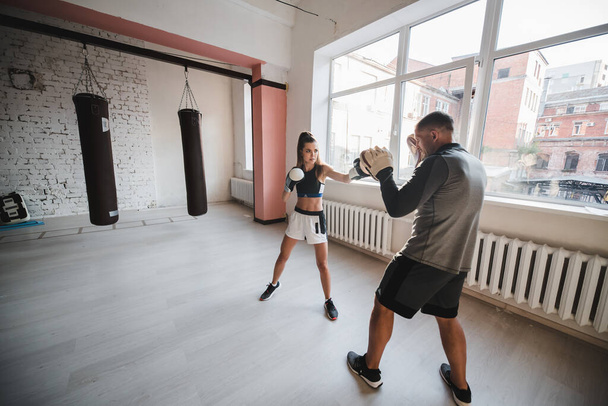 Ένας άντρας και μια γυναίκα εκπαιδεύονται στην αίθουσα εκπαίδευσης μαχητών με γάντια πυγμαχίας και πατούσες. - Φωτογραφία, εικόνα