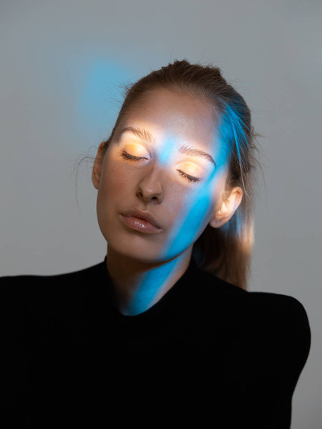 Portrait of young woman with neon blue light on her pretty face and closed eyes - Foto, immagini