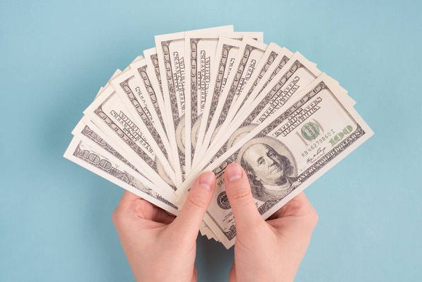 Вгорі над головою - фото жіночих рук, які тримають купу американських грошей над таблицею з ізольованим кольоровим фоном. - Фото, зображення