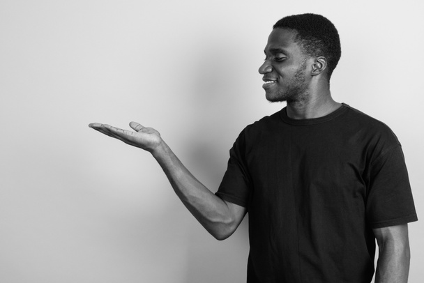 Στιγμιότυπο του νεαρού Αφρικανού άνδρα που φοράει μαύρο πουκάμισο με γκρι φόντο σε μαύρο και άσπρο - Φωτογραφία, εικόνα