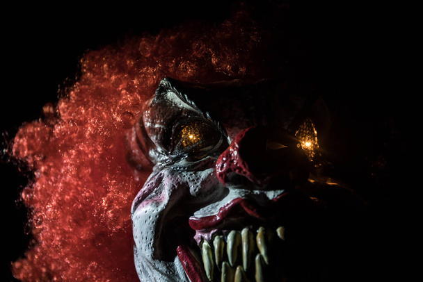 Straszna głowa klauna na drewnianym stole. Zły klaun uśmiechający się na ciemnym mglistym tle. Koncepcja Halloween. Skupienie selektywne - Zdjęcie, obraz