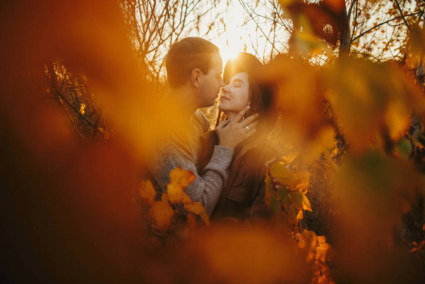 Stílusos pár ölelkezik az arany őszi levelek között meleg naplemente fényben. Fiatal, divatos férfi és nő gyengéden ölelkeznek az őszi fánál. Romantikus érzéki pillanat - Fotó, kép