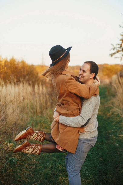 Feliz pareja elegante bailando en el prado de otoño en la cálida luz del atardecer. Momento sensual romántico. Joven mujer emocional y hombre sonriendo y girando en el campo de otoño - Foto, imagen