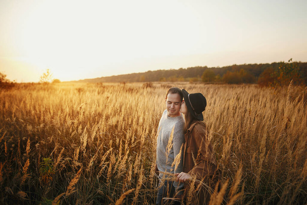 Couple élégant embrassant dans la lumière du coucher du soleil chaud dans le champ d'automne. Jeune femme à la mode et homme embrassant et embrassant parmi l'herbe et les herbes au soleil. Moment romantique authentique - Photo, image
