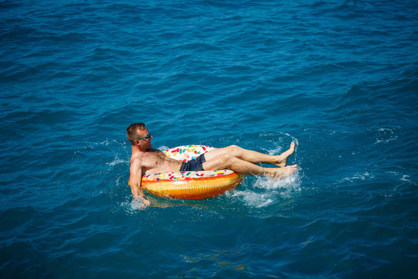 Un joven nada en mar abierto en un anillo inflable en un día soleado. Vacaciones de verano, turista de vacaciones - Foto, imagen