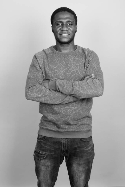Studioaufnahme eines jungen Afrikaners, der ein langärmeliges Hemd vor grauem Hintergrund in schwarz-weiß trägt - Foto, Bild