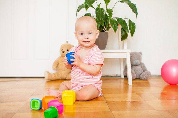 Little baby girl sitting on the floor, crawling and playing with brightly colored educational toys - Fotoğraf, Görsel