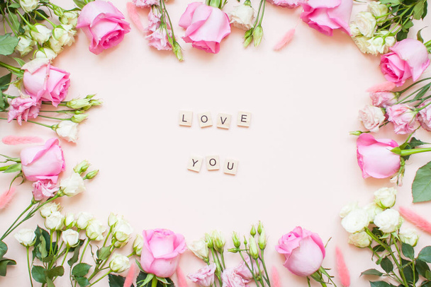 Inscription of wooden blocks love you. Frame of delicate white and pink roses and eustomas on a light pink background. Layout. - Fotografie, Obrázek
