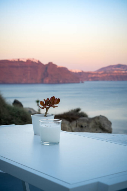 Свічка і прикраса рослин на білому столі. Оя, острів Санторіні, сірий. Чудові кольори заходу сонця на кальдері. Портретний формат - Фото, зображення