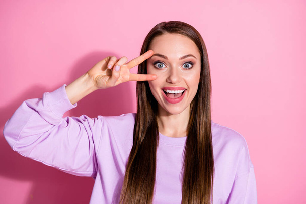 Photo of attractive cool cheerful lady showing two fingers v-sign symbol near eye say hi friends meeting party gathering wear casual purple sweater isolated pink pastel color background - Fotografie, Obrázek