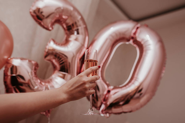 Die Hand der Frau hält ein Glas mit rosa Champagner vor dem Hintergrund gefälschter pinkfarbener Kugeln 30 - Foto, Bild