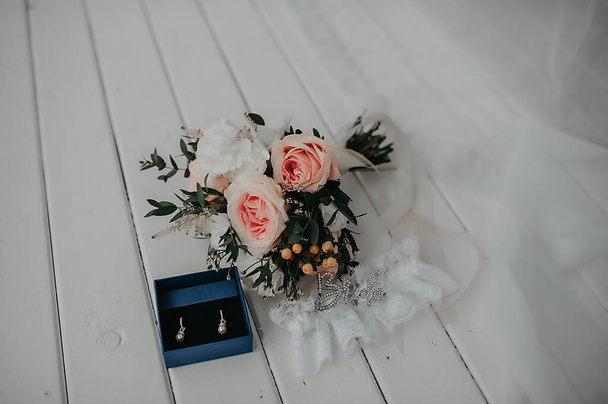 stylish accessories for the bride, feminine care and beauty items for the wedding day and the bride's outfit, expensive earrings with white gold diamonds and a bouquet of peony roses - Photo, Image