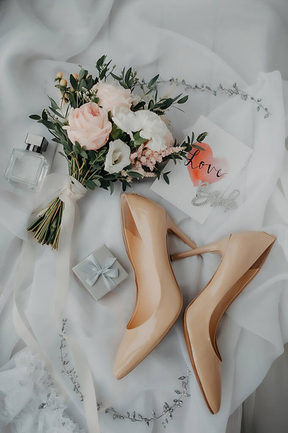 accesorios elegantes de la novia para vestirse y traje de boda, zapatos de charol beige, caja de plata para anillos y un elegante ramo de rosas peonias sobre un fondo de tul blanco - Foto, Imagen