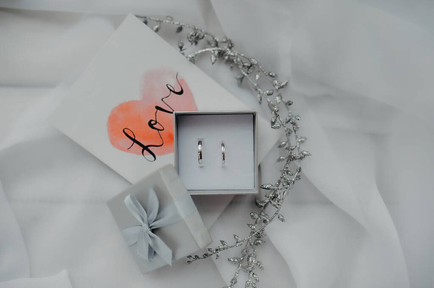 romantische kaart, eenvoudige gladde witgouden ringen in een zilveren doos op de achtergrond van een foto met de inscriptie liefde en witte tule - Foto, afbeelding