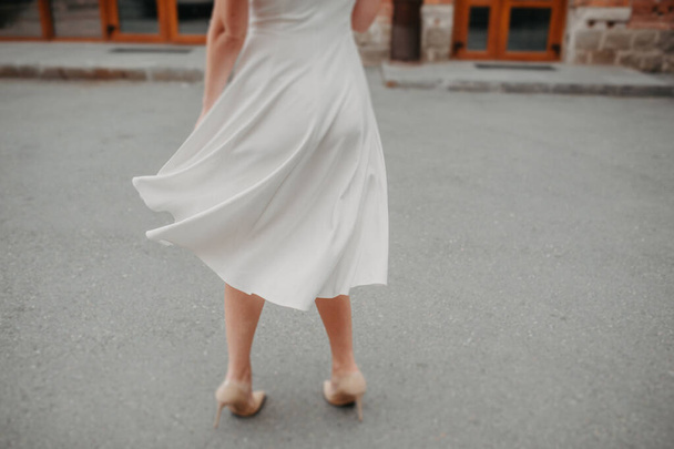 kobieta bez twarzy w białej prostej sukience o długości midi wiruje i sukienka wiruje w różnych kierunkach na ulicy przeciwko asfaltowi - Zdjęcie, obraz
