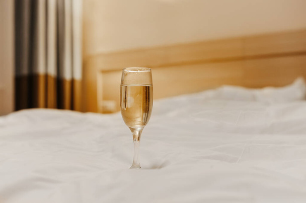 lonely glass goblet with a light drink on a pure white crumpled bed - Photo, Image