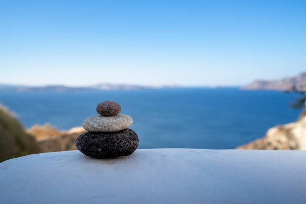 Close-up shot of pebbles stacked on each other in a balance with santorini caldera in the background - Photo, Image