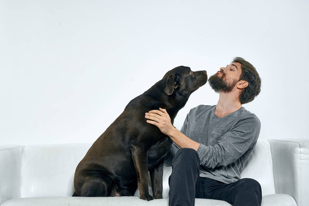 Ο άνθρωπος με ένα σκυλί συντροφιάς στον καναπέ διασκέδαση φίλους συναισθήματα φως δωμάτιο - Φωτογραφία, εικόνα