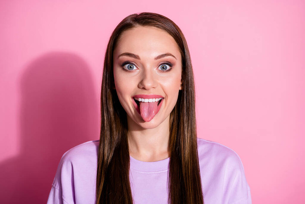 Closeup photo of attractive funky carefree lady sticking tongue out mouth teasing boyfriend playful girlish mood wear casual purple sweater isolated pink pastel color background - Фото, изображение