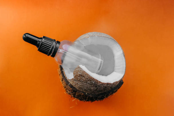 Noix de coco mûre cassée avec pulpe juteuse sur fond clair orange clair, pot en verre transparent avec capuchon pour cosmétiques ou médicaments dans une coque de noix de coco - Photo, image