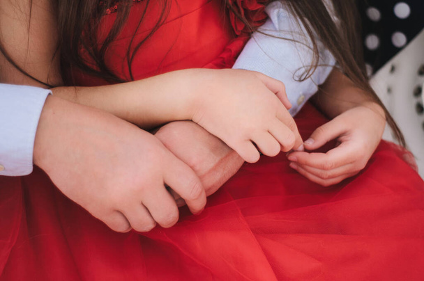 de handen van het kind en de handen van de ouders worden samengehouden op een rode achtergrond van tule kleding - Foto, afbeelding