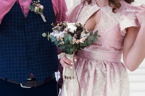 Braut und Bräutigam in ungewöhnlichen Brautkleidern und einem wunderschönen Blumenstrauß aus Baumwolle, einem rosa Kleid der Braut aus Jacarte und einem rosa Hemd des Bräutigams - Foto, Bild