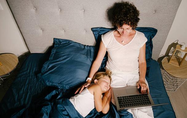Stock photo of young mother using laptop and lying in bed with her young daughter. - Photo, Image