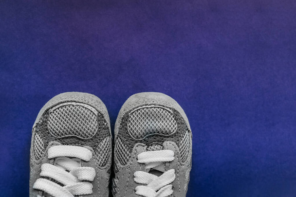 Nueva zapatillas de deporte fresco con estilo de un tamaño muy pequeño para un bebé recién nacido en gris con cordones blancos atados sobre un fondo púrpura de neón brillante y un lugar vacío para una inscripción - Foto, imagen