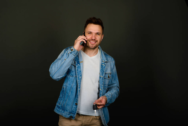 Hombre joven guapo en ropa casual inteligente sosteniendo el teléfono inteligente y mirando a la cámara con sonrisa - Foto, Imagen