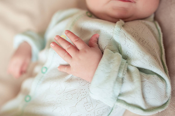 kleine mooie pennen met lange nagels in een pasgeboren baby in lichte muntkledij op een gezellige plaid - Foto, afbeelding