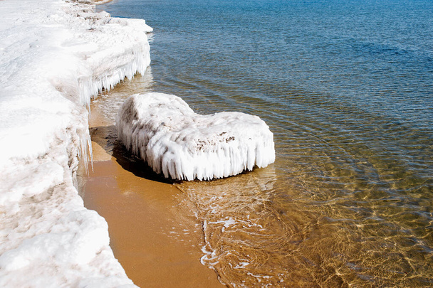 El témpano de hielo insólito en forma de corazón - la postal ideal para el Día de San Valentín, el mar invernal con la orilla congelada, la arena amarilla y el mar frío azul claro - Foto, Imagen