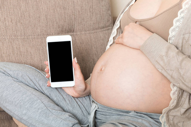 Pregnant woman showing smartphone with black screen in sofa. - Zdjęcie, obraz