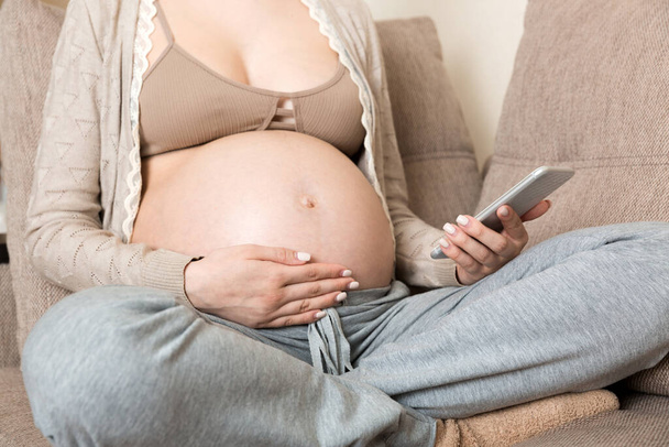 Kaukázusi terhes lány mobiltelefon, pihen az ágyon otthon. - Fotó, kép