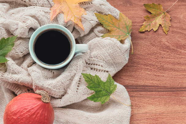 Ένα φλιτζάνι καφέ στο τραπέζι με κολοκύθα, φθινοπωρινά φύλλα και ένα πλεκτό πουλόβερ. Φθινοπωρινή ιδέα, κορυφαία προβολή. - Φωτογραφία, εικόνα