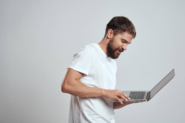 Un hombre con un portátil en sus manos sobre un fondo claro en una camiseta blanca emociones fondo claro nuevas tecnologías - Foto, imagen