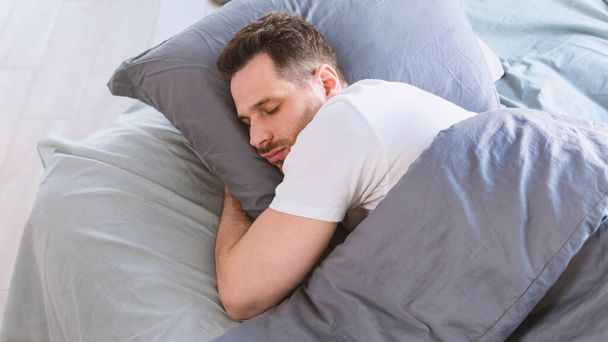 Man Sleeping Hugging Pillow Lying In Bed Resting In Bedroom - 写真・画像
