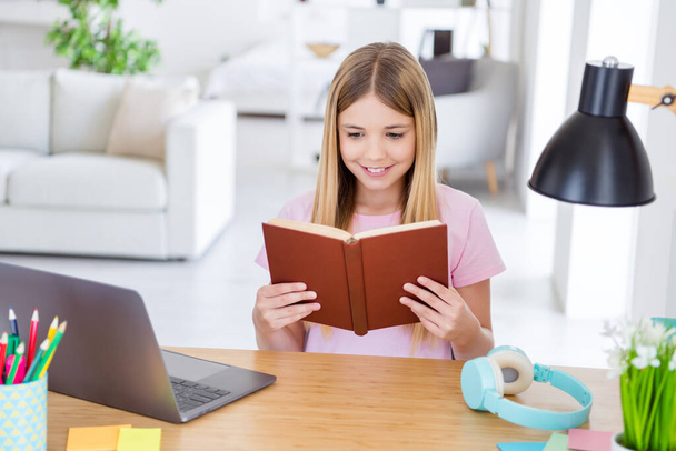 Photo of positive kid girl sit table desk study remote prepare exam read book in house indoors living apartment - Foto, afbeelding