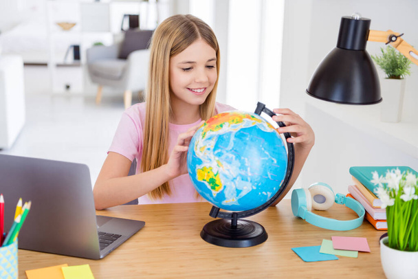 Photo of positive kid girl sit table desk study remote homeschool geography explore globe continent in house indoors - Фото, зображення