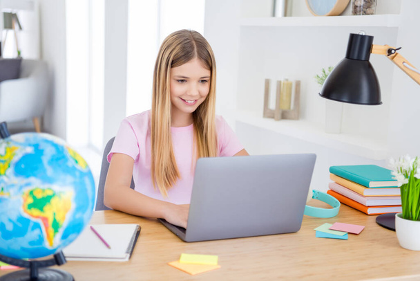 Photo of positive kid girl sit table desk study remote use smartphone have online communication lesson with tutor in house indoors - Fotografie, Obrázek