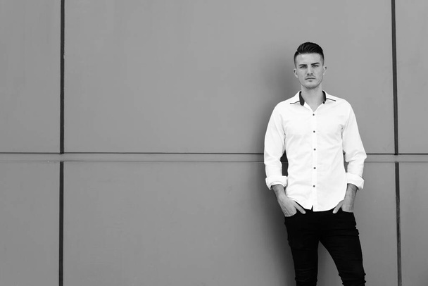Fiatal, jóképű spanyol üzletember portréja fekete-fehér betonfalon - Fotó, kép