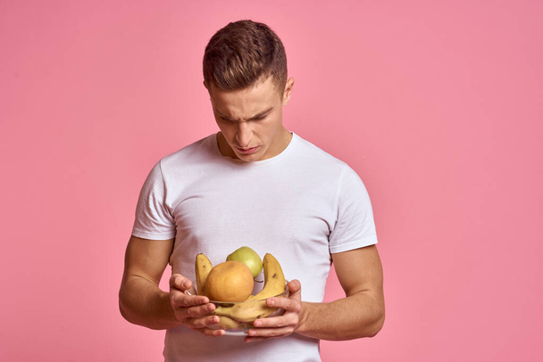 Мужчина с фруктами в руках на розовом фоне - Фото, изображение