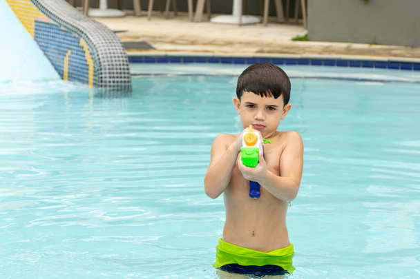 6 jaar oud jongen richt zijn waterpistool op de camera. - Foto, afbeelding